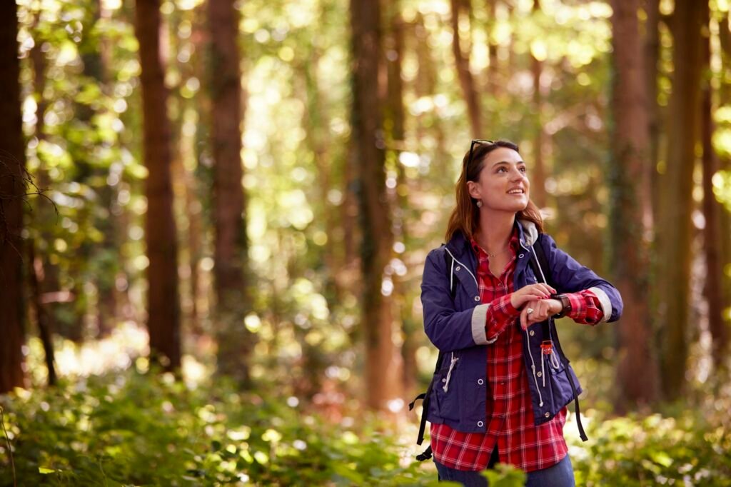 Woman On Holiday Hiking Through Woods Using GPS App On Smart Watch To Navigate